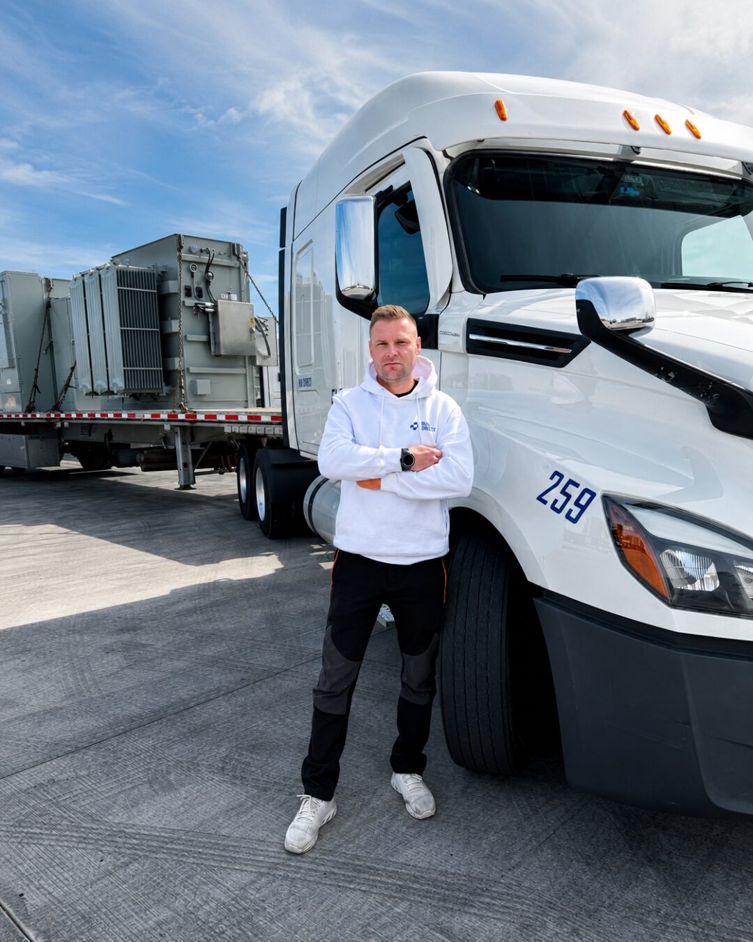Run Direct driver in a branded hoodie next to his flatbed loaded with an industrial transformer